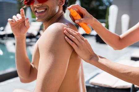 Cropped view of woman applying sunscreen on back of smiling friend outdoors