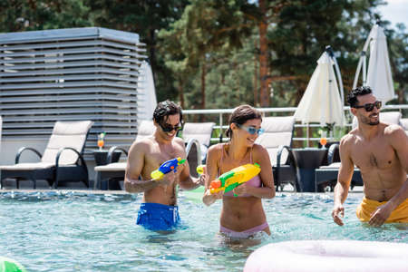 happy young woman with interracial men playing with water guns in swimming pool