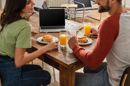 Smiling woman sitting near boyfriend, tasty pancakes and laptop at home