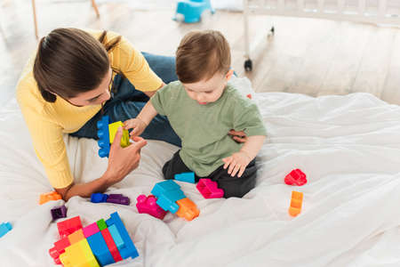 High angle view of mother and son playing building blocks on beddingの写真素材