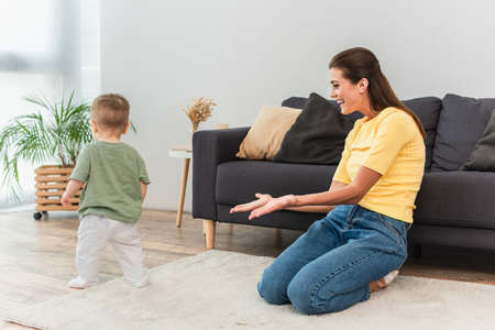 Smiling mother pointing at toddler child on carpet at home