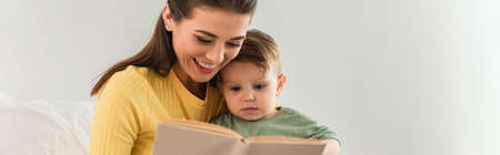 Young mother and child reading book near pillow at home, bannerの写真素材