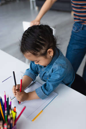 Asian girl drawing near blurred color pencils and parent at homeの写真素材