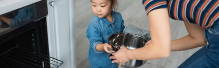 Mother holding pan near asian daughter and oven at home, bannerの写真素材