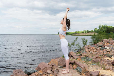 full length of young woman in sportswear practicing yoga near seaの写真素材