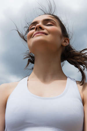 low angle view of young smiling woman in crop top against blue sky with cloudsの写真素材