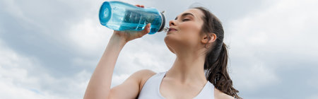 low angle view of young woman in crop top drinking water against blue sky with clouds, banner