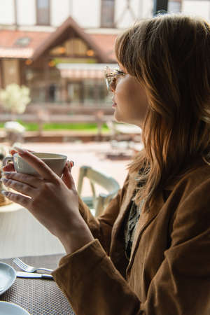 Side view of young stylish woman holding coffee cup in cafeの写真素材