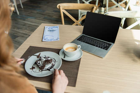 Laptop and coffee near blurred woman with dessert in cafeの写真素材