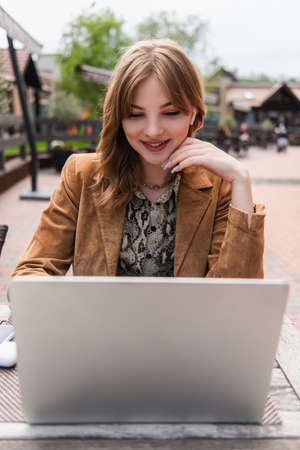 Stylish blogger in earphone using blurred laptop on terraceの写真素材