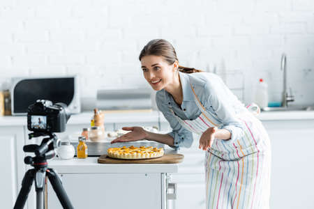 happy culinary blogger pointing with hands at delicious pie near blurred digital camera
