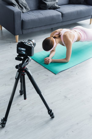 digital camera on tripod near sportswoman training in plank pose on fitness matの写真素材