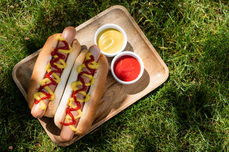 top view of wooden tray with hot dogs, mustard and ketchup on green grassの写真素材
