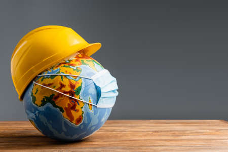medical mask and hardhat on globe on wooden surface isolated on gray, labor day conceptの写真素材