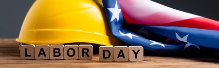 cubes with labor day lettering near helmet and usa flag on wooden surface isolated on gray, banner