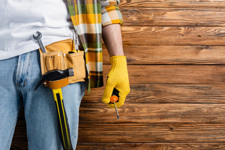cropped view of workman in tool belt holding screw driver on wooden backgroundの写真素材