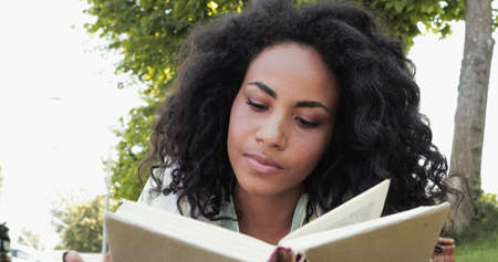 curly african american woman reading book in hardcover