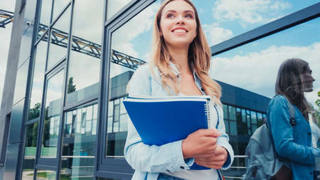 joyful young student holding notebooks near building