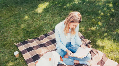 high angle view of student reading book on checkered blanket in park