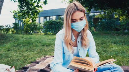 Student in medical mask reading book in parkの写真素材