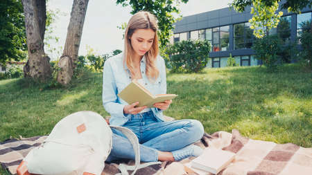 young woman with crossed legs sitting on blanket and reading book