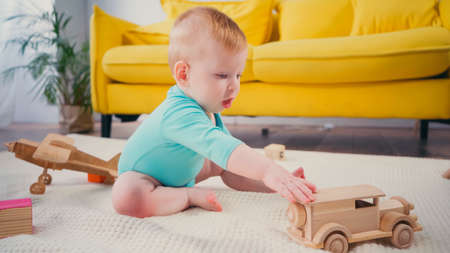 barefoot baby boy sitting on blanket and playing with wooden toy carの写真素材