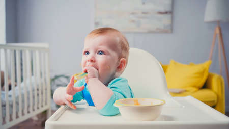 infant boy with blue eyes sitting in feeding chair and eating baby foodの写真素材