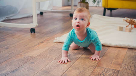 surprised infant boy crawling on floor in living roomの写真素材