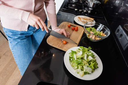 cropped view of woman cutting cherry tomatoes near fried chicken fillet while preparing breakfastの写真素材