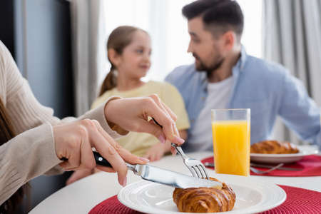 woman cutting tasty croissant near husband and daughter on blurred backgroundの写真素材