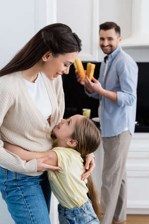 blurred man with bread smiling in kitchen near hugging wife and daughterの写真素材