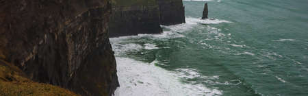 scenic view of rocky coastline and blue sea waves with foam, banner
