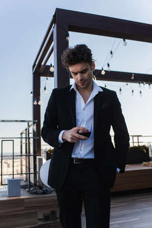 elegant man in suit holding glass of wine on terrace