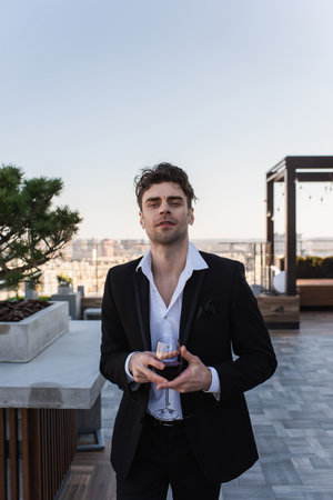 elegant man in suit holding glass of red wine on terrace