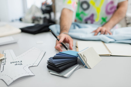 partial view of blurred designer holding pen near sewing pattern and color palette