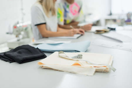 selective focus of fabric samples and measuring tape near blurred fashion designers, cropped viewの写真素材