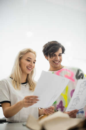 joyful designer looking at drawings in atelier on blurred foregroundの写真素材