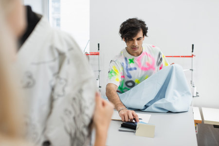 stylish designer choosing fabric and colors near colleague and mannequin on blurred foreground