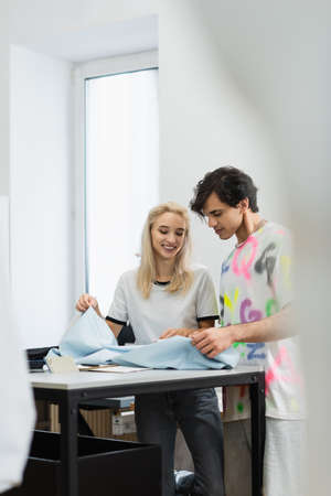 smiling fashion designers looking at sample of tissue on blurred foreground
