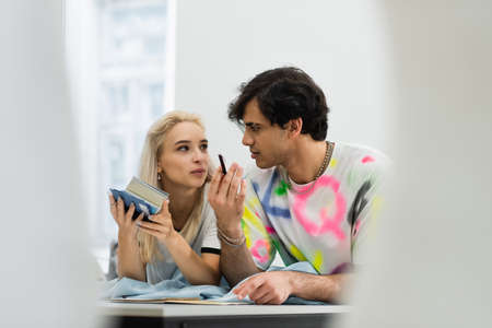 stylish designer talking to colleague holding color palette in atelier, blurred foreground