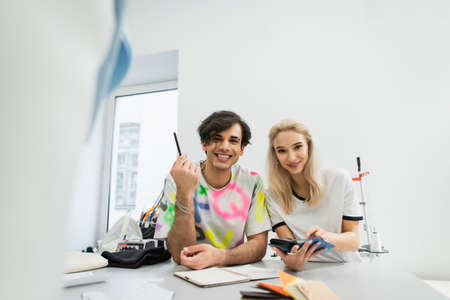 smiling fashion designers looking at camera while choosing colors from palette on blurred foregroundの写真素材