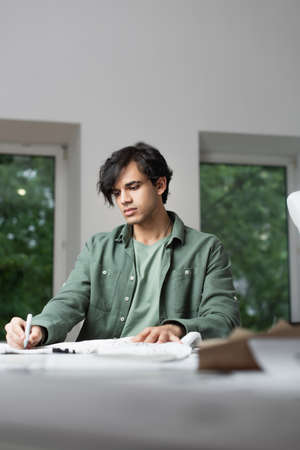 young fashion designer drawing on tissue with felt pen on blurred foreground