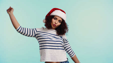 young woman in santa hat pouting lips isolated on blue