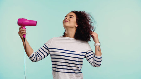 happy young woman drying curly hair isolated on blueの写真素材