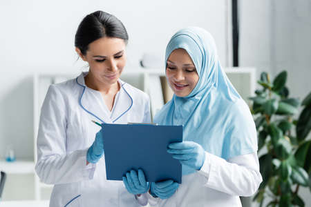 Smiling arabian doctor holding clipboard near colleagueの写真素材