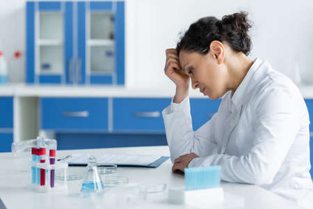 Side view of upset african american scientist looking at petri dishes in lab