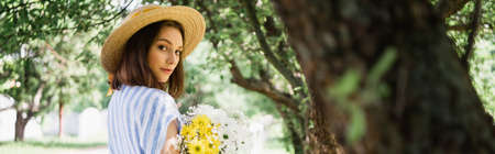Young woman in straw hat holding bouquet in park, bannerの写真素材