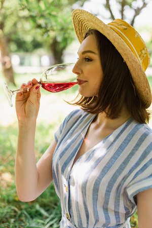 Side view of woman in sun hat drinking wine in park