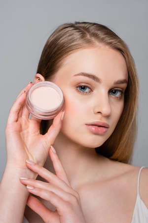 young woman holding container with face powder isolated on grayの写真素材