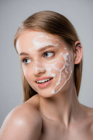 young woman with blue eyes and cleansing foam on face isolated on grayの写真素材